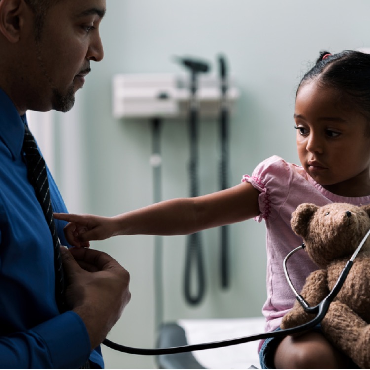 a little girl holding a teddy bear with a stethoscope pointing to the heart of a man.