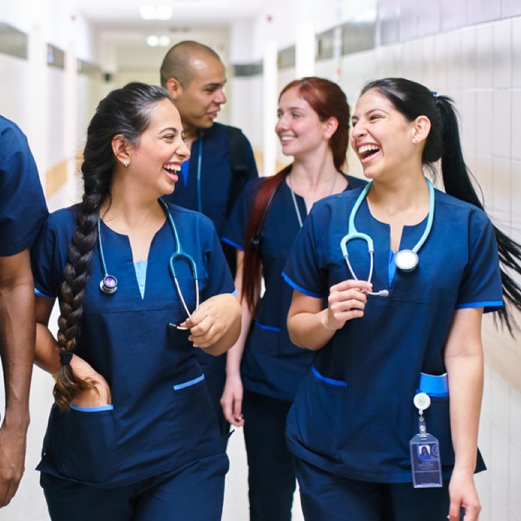 a group of people laughing and talking. They are all wearing blue scrubs and stethoscopes.